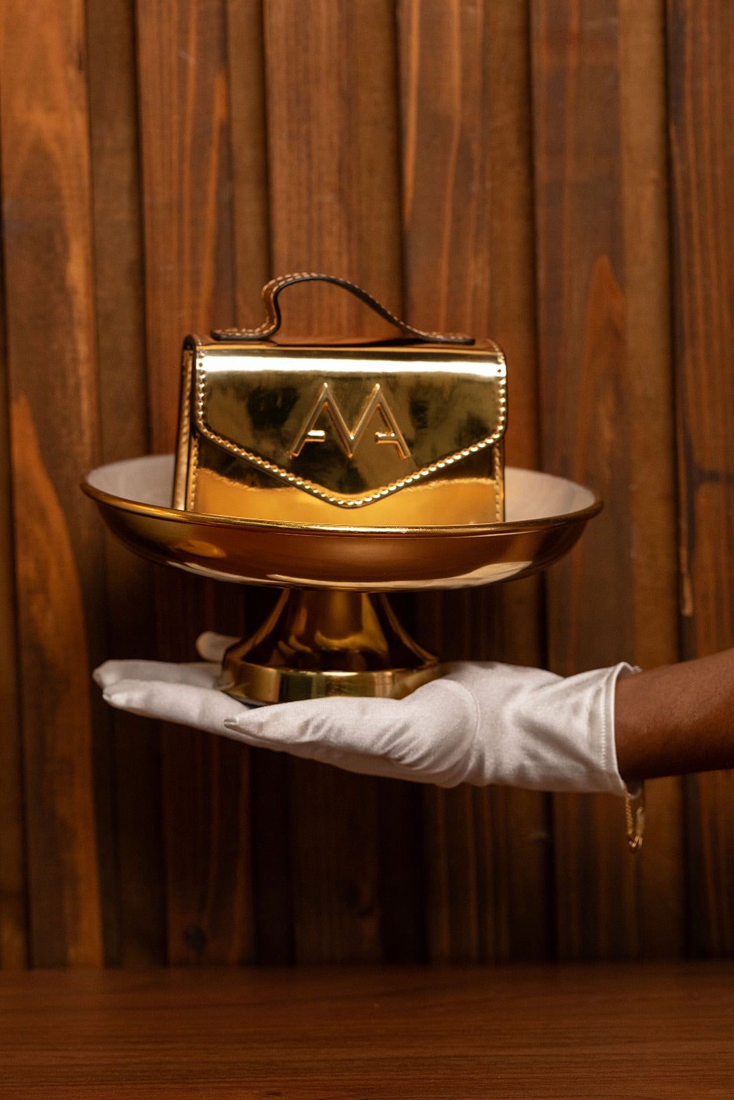 Gold handbag with a logo held by a gloved hand against a wooden background