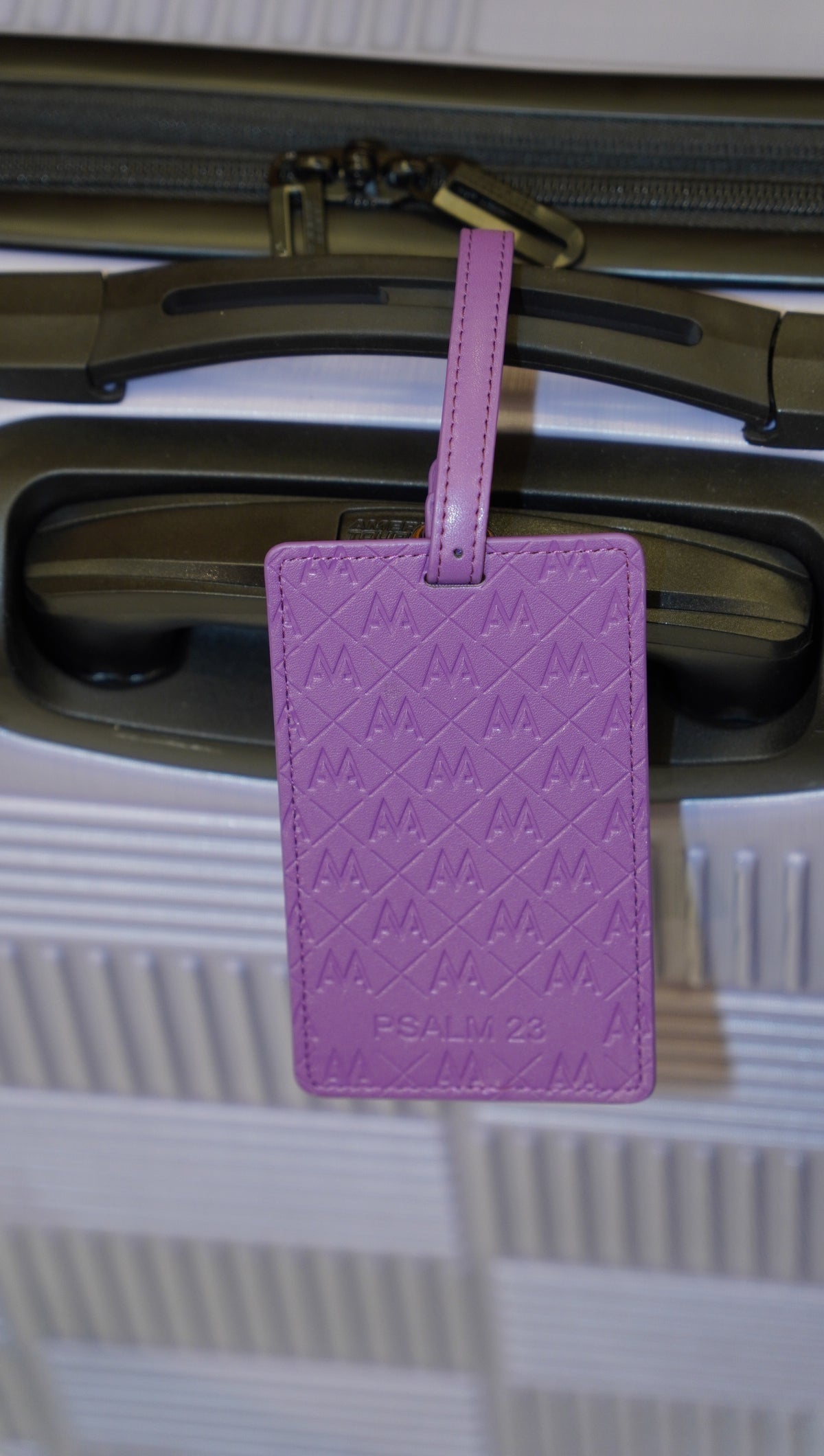 A purple quilted leather luggage tag with an embossed geometric pattern and the brand name 'PSALM 22' at the bottom, hanging from a suitcase handle.