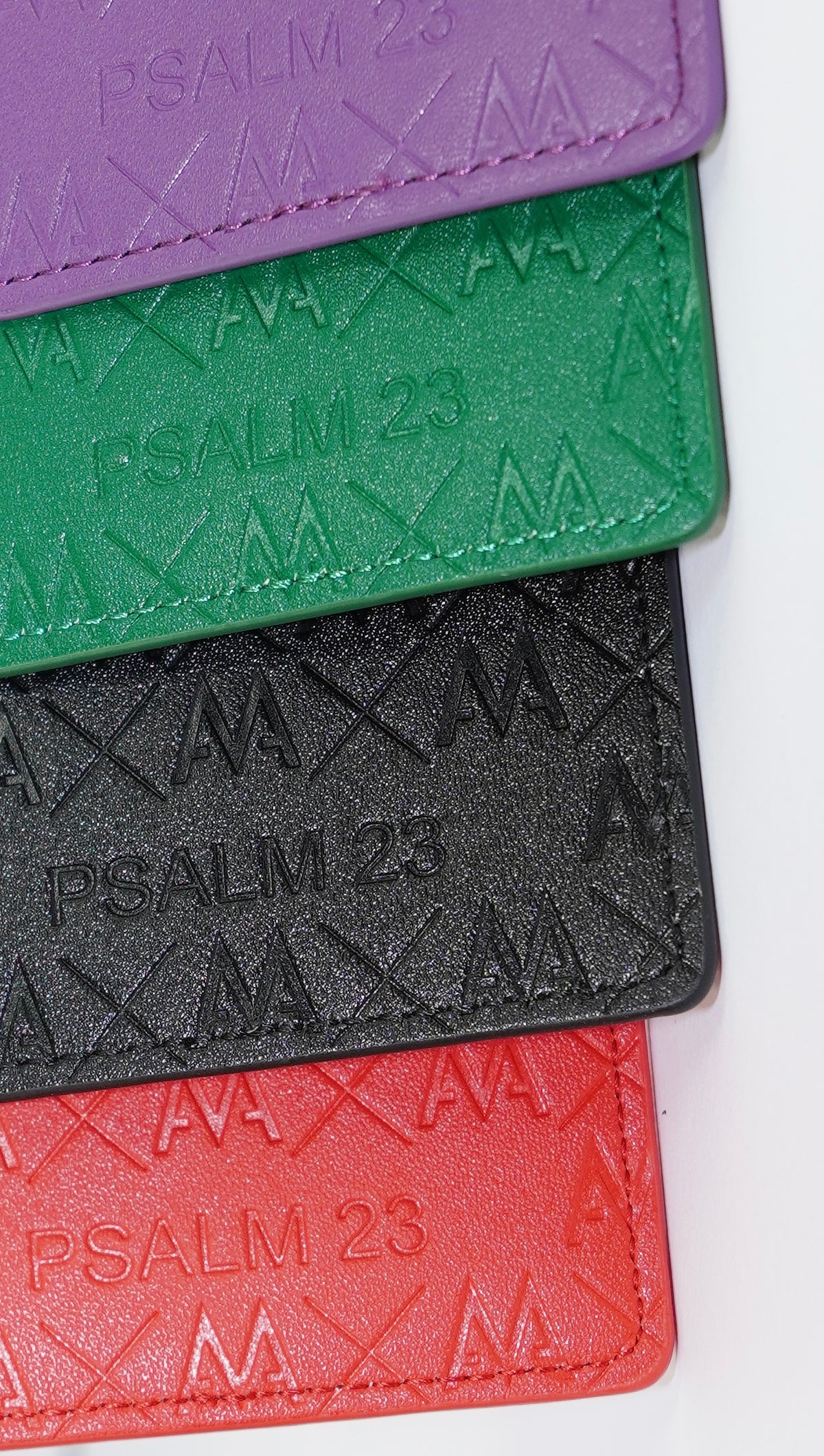 Four embossed leather cardholder or wallet pieces stacked vertically on a white background, in purple, green, black, and red, each embossed with 'PSALM 23'.