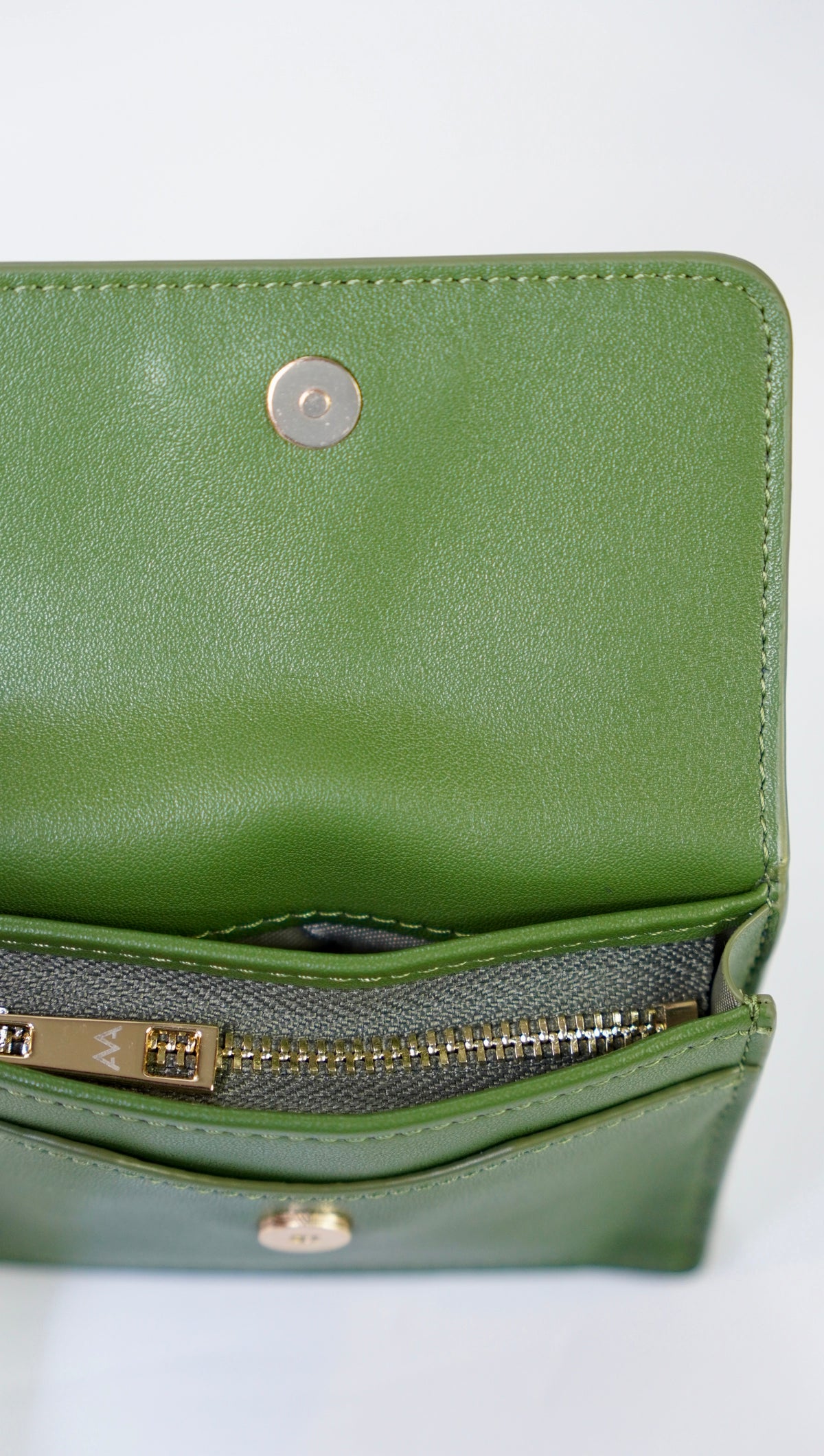 A close-up of an olive green leather wallet or clutch shown open, revealing a gray zippered pocket with gold-tone hardware and a silver snap button on the inside flap.