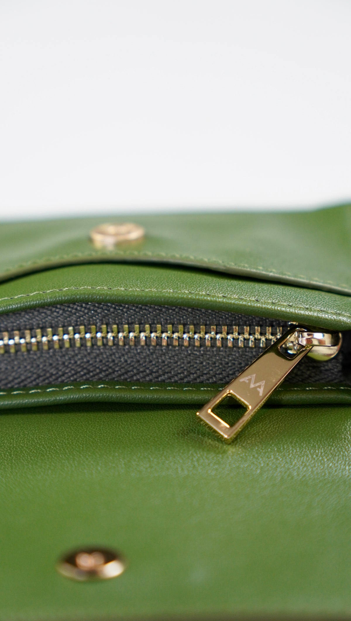 Close-up of an olive green leather zipper pouch with gold-tone hardware and a black mesh interior lining.