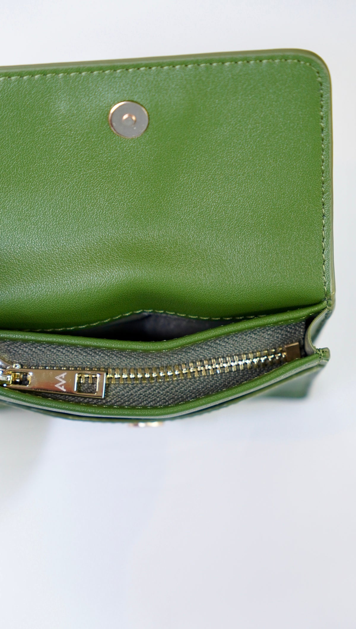 A close-up of a green leather wallet or clutch shown open, revealing a zippered interior with gold-tone hardware on a white background.